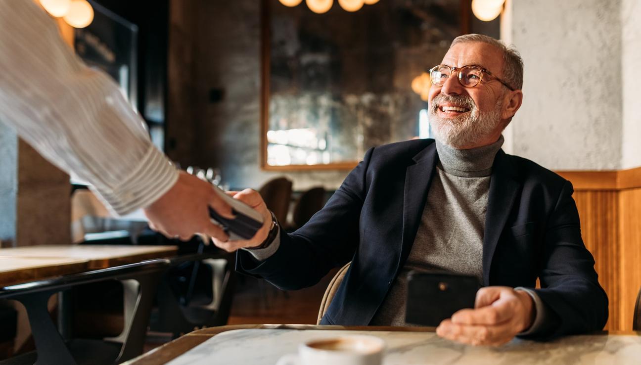 Man med grått skägg betalar med sitt kreditkort på restaurangen