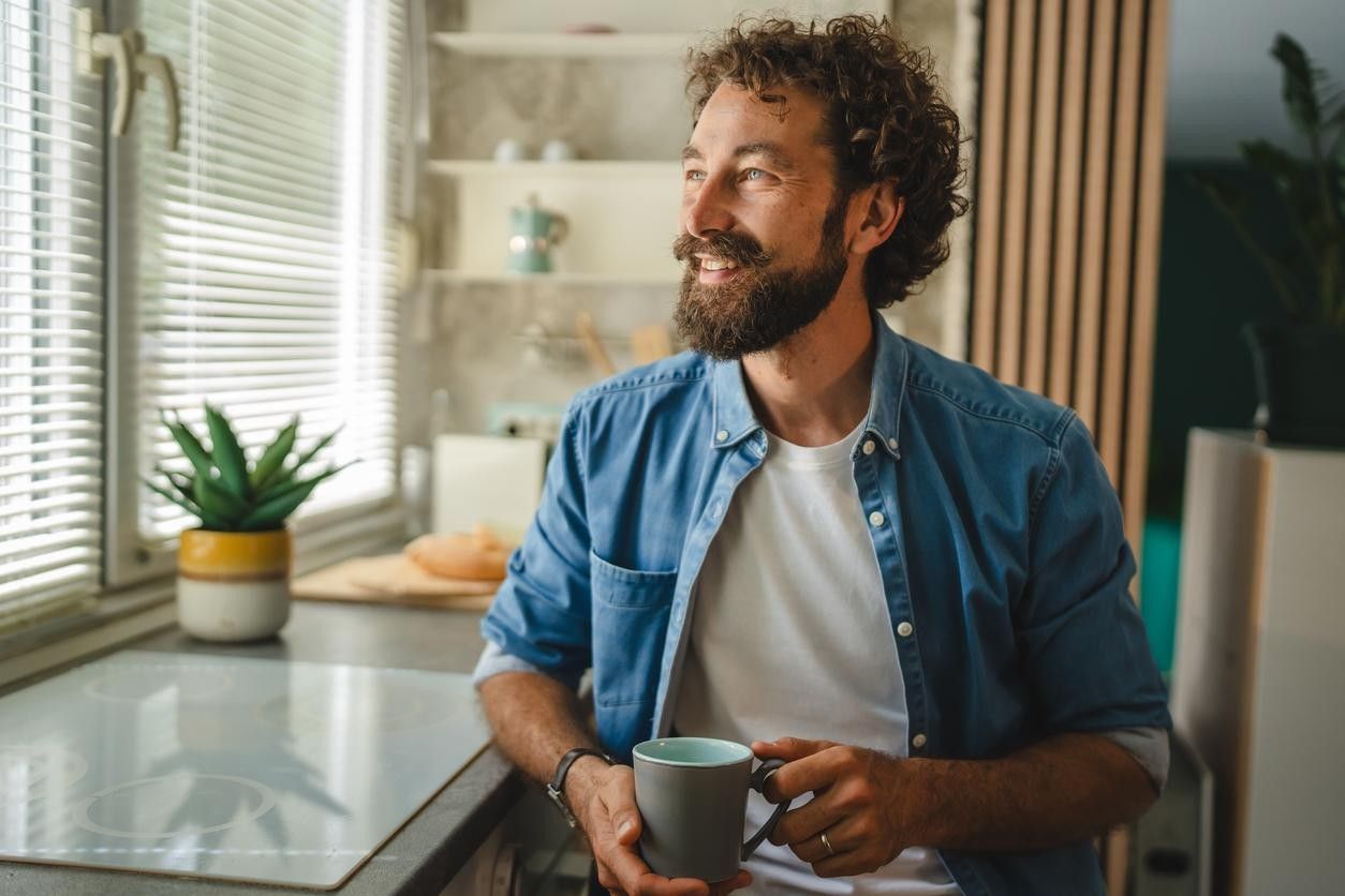 Mann med kaffekopp ser ut av vinduet. bilde.