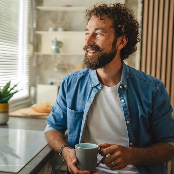 Mann med kaffekopp ser ut av vinduet. bilde.