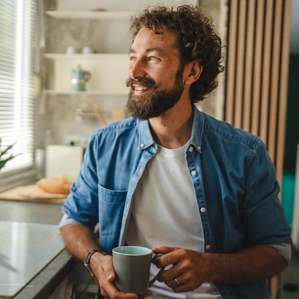 Mann med kaffekopp ser ut av vinduet. bilde.