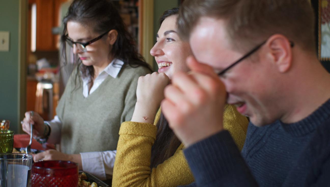 Ett gäng vänner sitter runt ett bord, äter och skrattar.