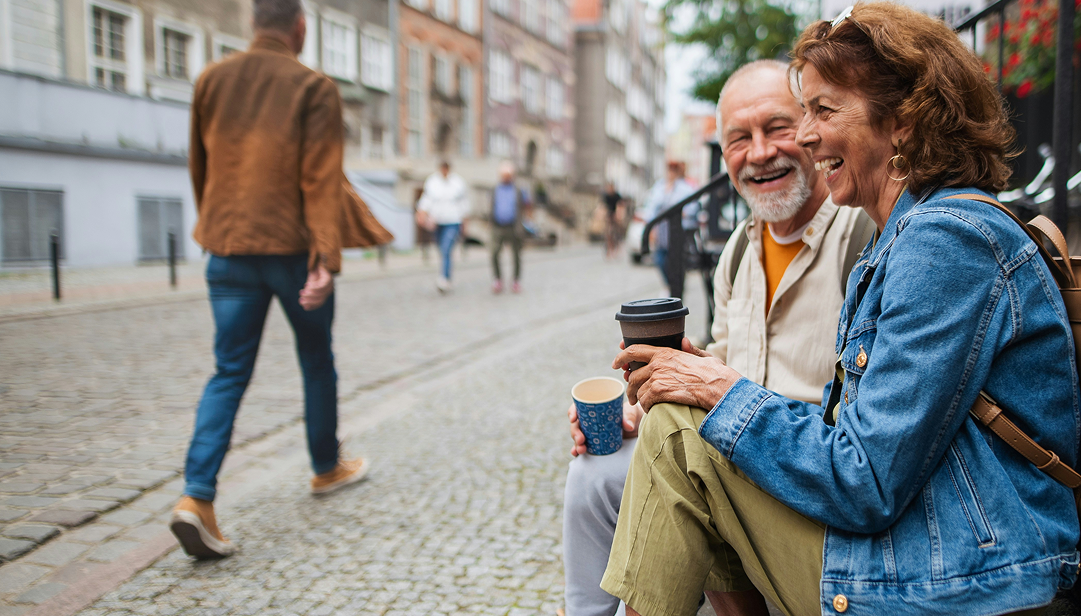 Par sitter i trappen ute mot fortauet. De har kaffe i hånden og smiler. bilde.
