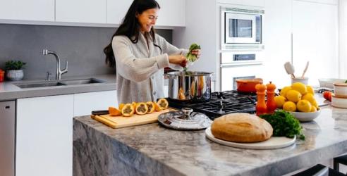 En kvinna står i köket och lagar mat, med grytor och matvaror framför sig