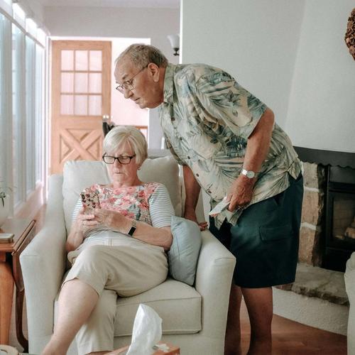 Ett äldre par sitter i vardagsrummet och ser på mobilen