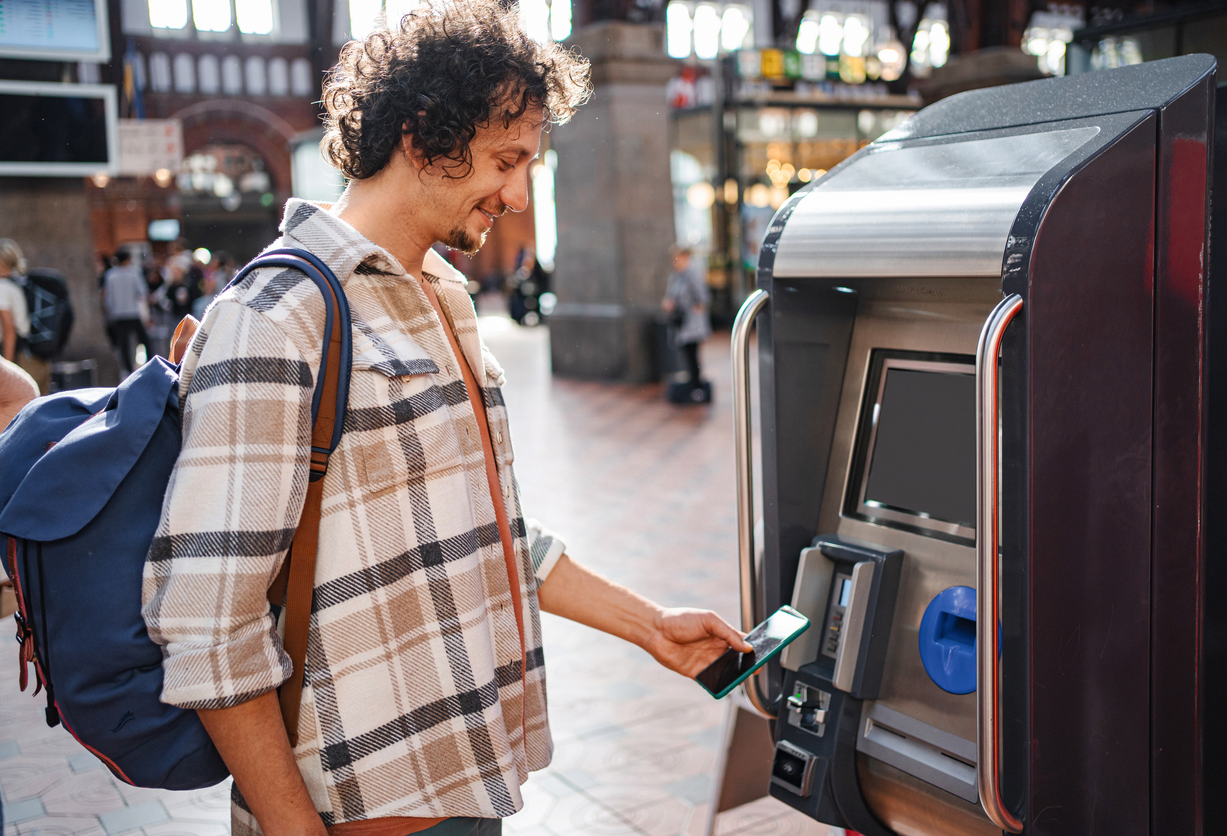En mann kjøper togbillett og betaler med Morrow Bank kredittkort i mobilen. bilde,
