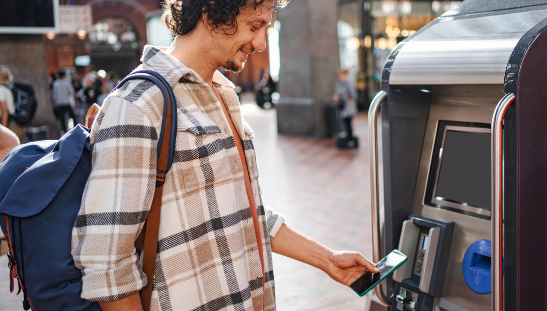 En mann kjøper togbillett og betaler med Morrow Bank kredittkort i mobilen. bilde,