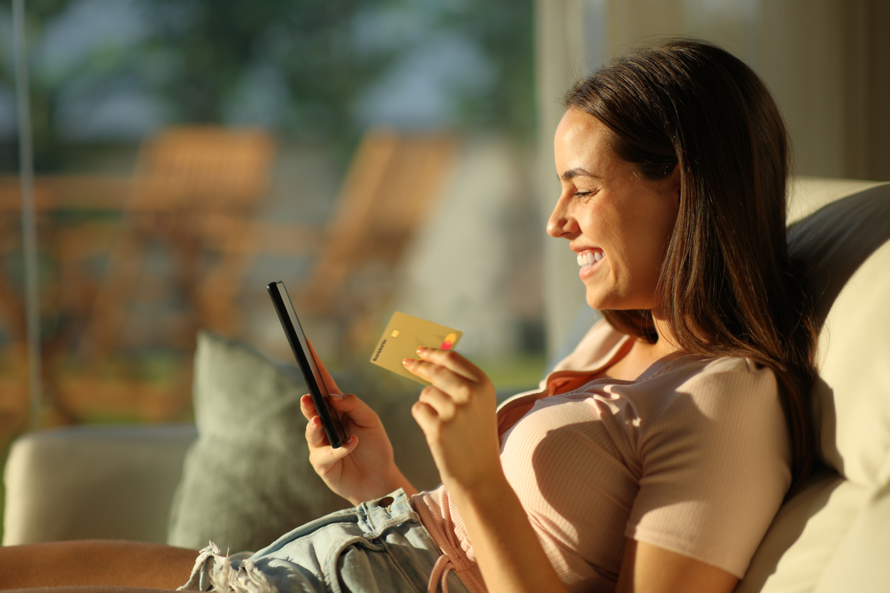 Dame sitter i sollyys med Morrow kredittkort i ene hånden og mobilen i den andre. bilde.