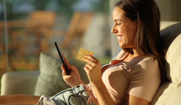 Dame sitter i sollyys med Morrow kredittkort i ene hånden og mobilen i den andre. bilde.