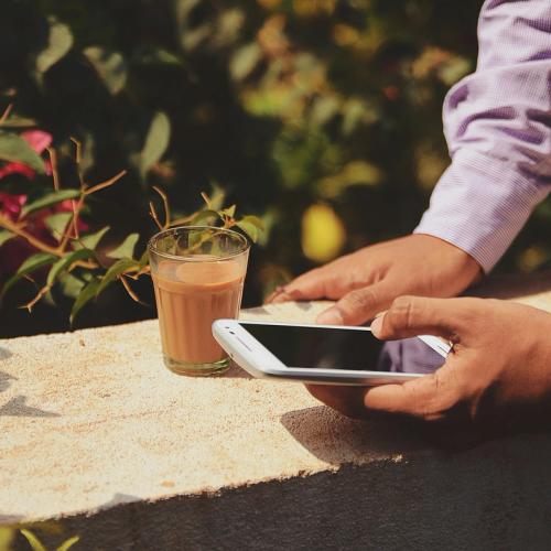 Armar som håller en mobil och lutar sig mot en mur. Ett glas kaffe står brevid.