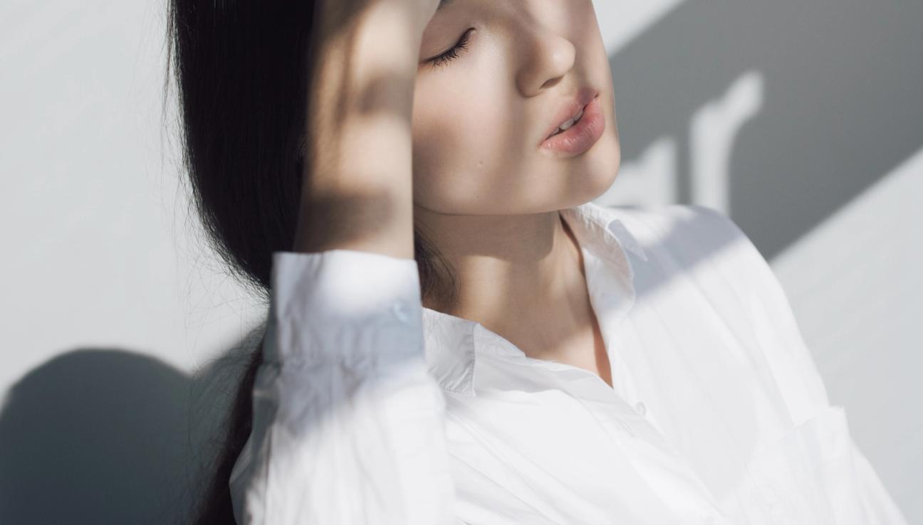 A girl is leaning her head in her hands while keeping her eyes closed. The sunlight is shining on her, and she looks peaceful.