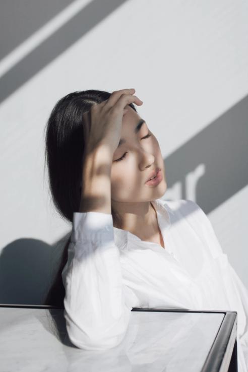 A girl is leaning her head in her hands while keeping her eyes closed. The sunlight is shining on her, and she looks peaceful.
