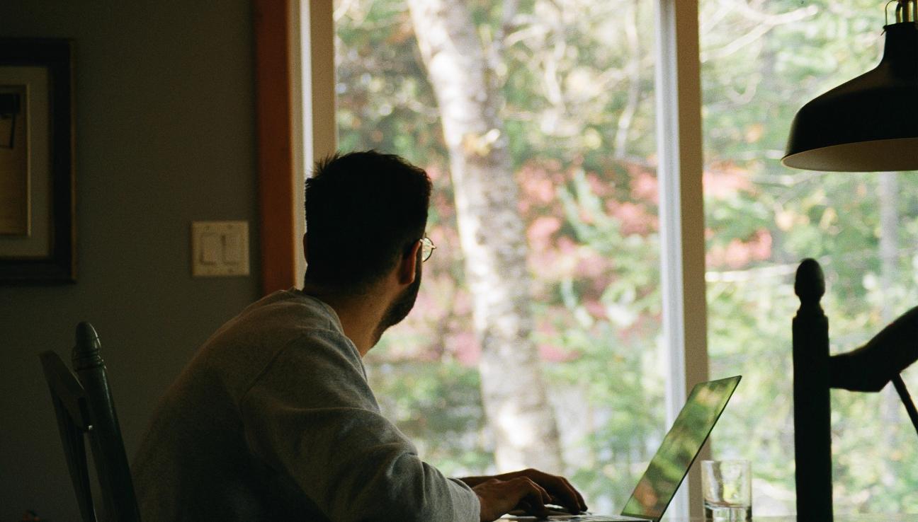 A man working on his computer and looking out the window.