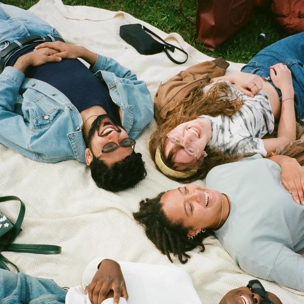 Four friends lying on a picnic blanket in the grass. They are all smiling and laughing.