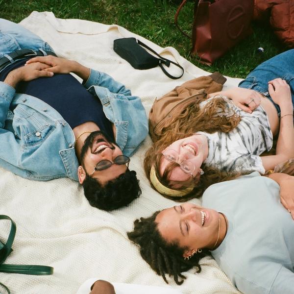 Four friends lying on a picnic blanket in the grass. They are all smiling and laughing.