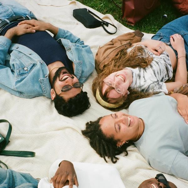 Four friends lying on a picnic blanket in the grass. They are all smiling and laughing.