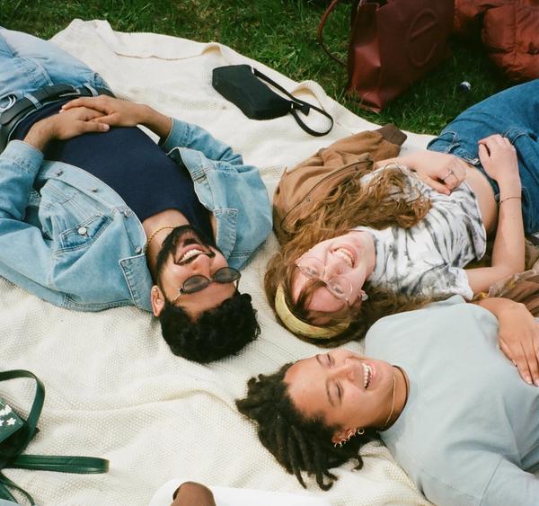 Four friends lying on a picnic blanket in the grass. They are all smiling and laughing.