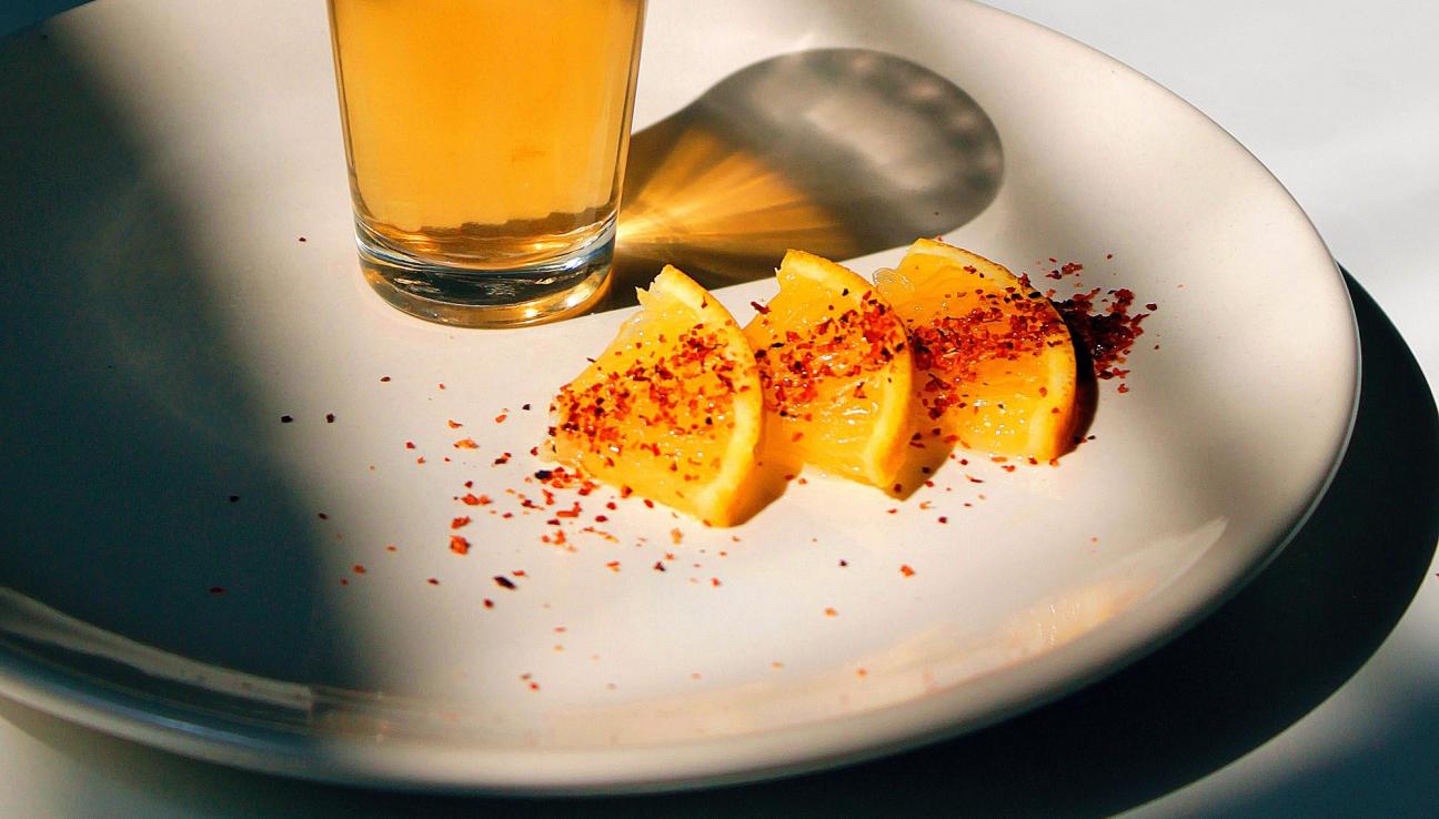 A plate with a glass of apple juice and oranges