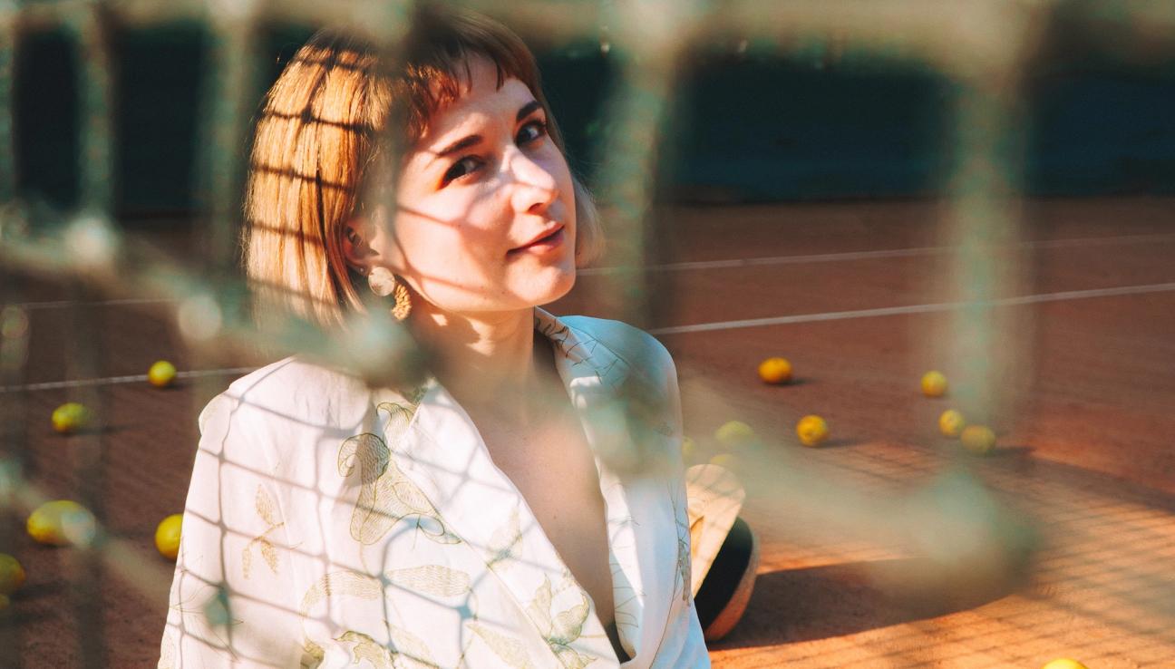 A woman is sitting on a tennis court in a white dress. It looks like there are tennis balls around her, but upon further inspection - they are apples.