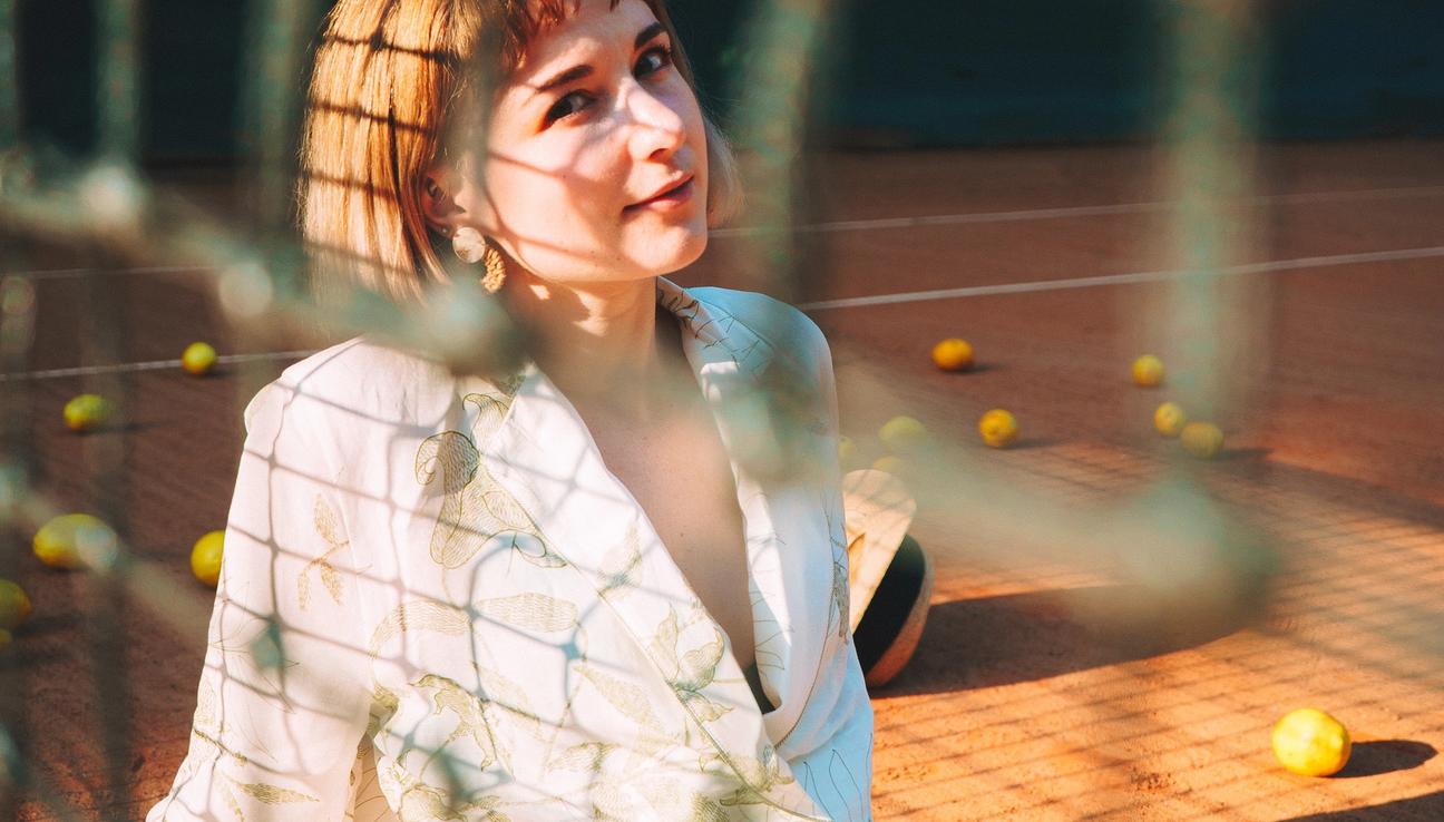 A woman is sitting on a tennis court in a white dress. It looks like there are tennis balls around her, but upon further inspection - they are apples.