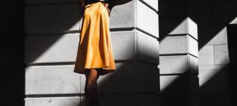 Woman in a yellow dress standing in direct sunlight and covering her eyes from the sun.