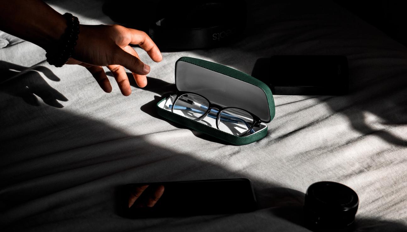 A hand reaching for a pair of glasses that are placed in sunlight.