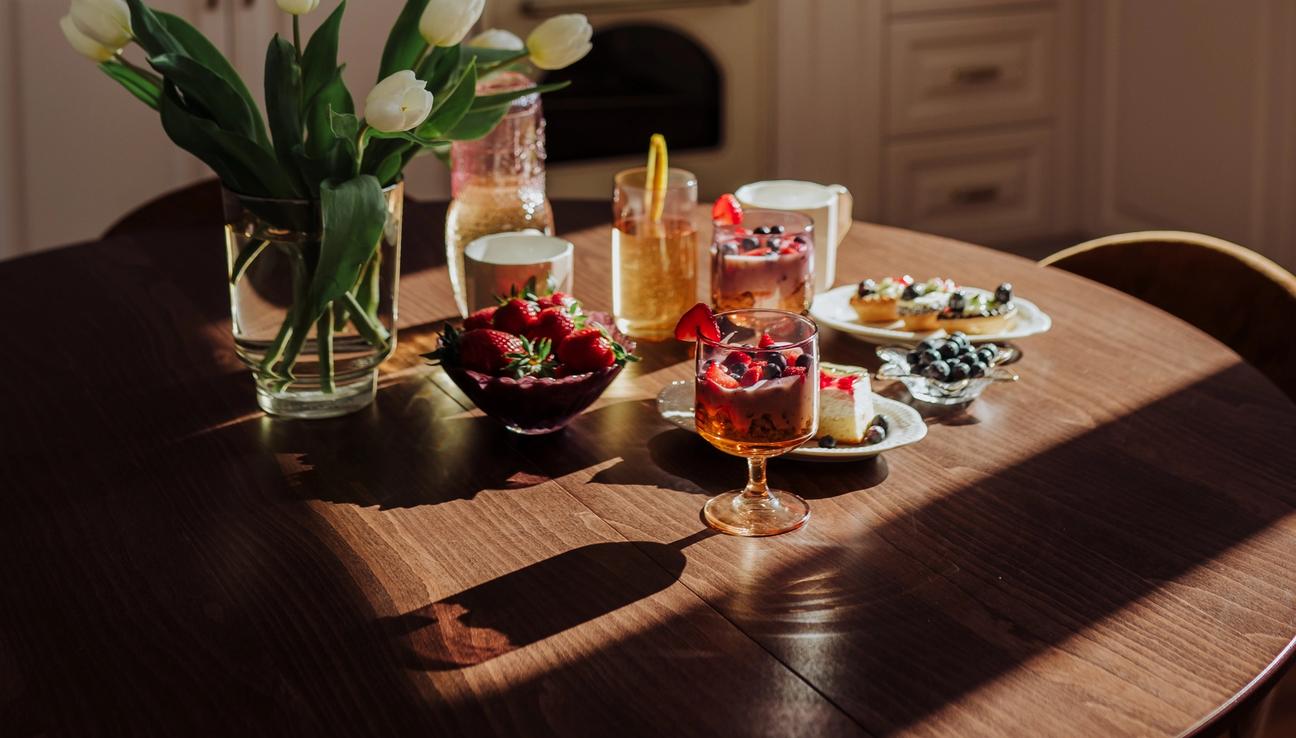 A kitchen table with white tulips and plates and glasses with juice and fresh berries