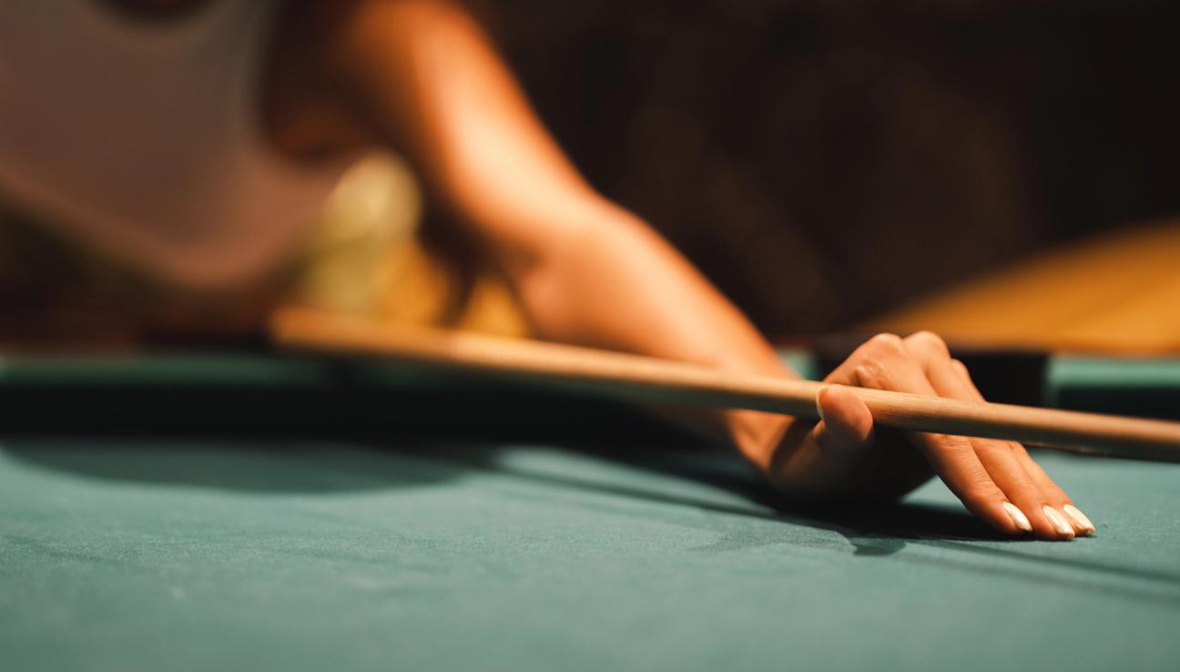 A woman with white nailpolish playing billiards