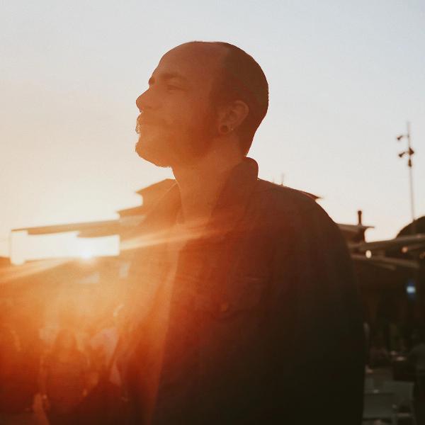 A man standing and taking a break in a crowd. The sun is setting.
