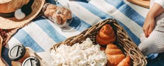 A picnic basket filled with croissants and flowers on a blue and white striped picnic blanket