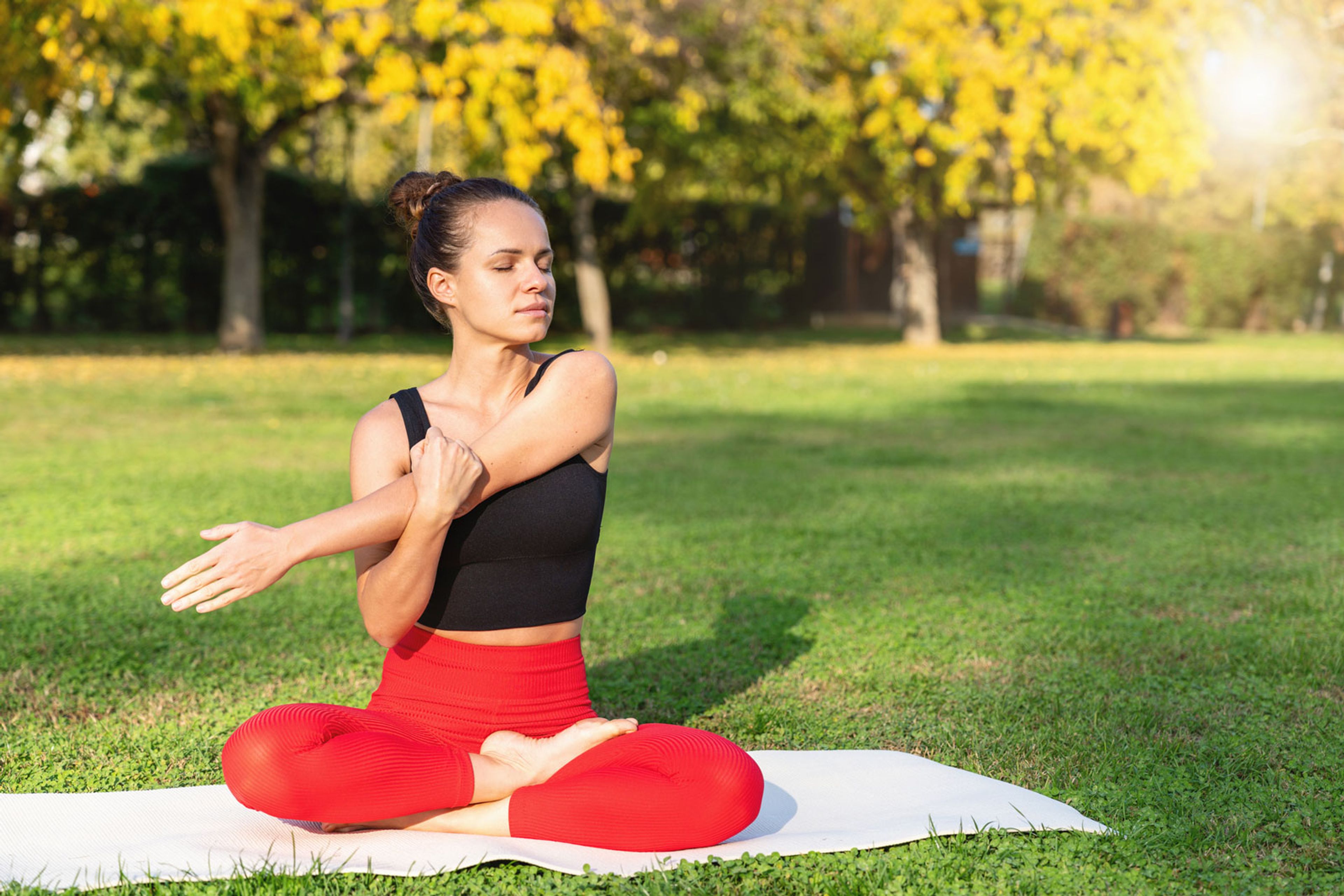 Two week wait tips: Young woman practices gentle arm stretches on a yoga mat outside