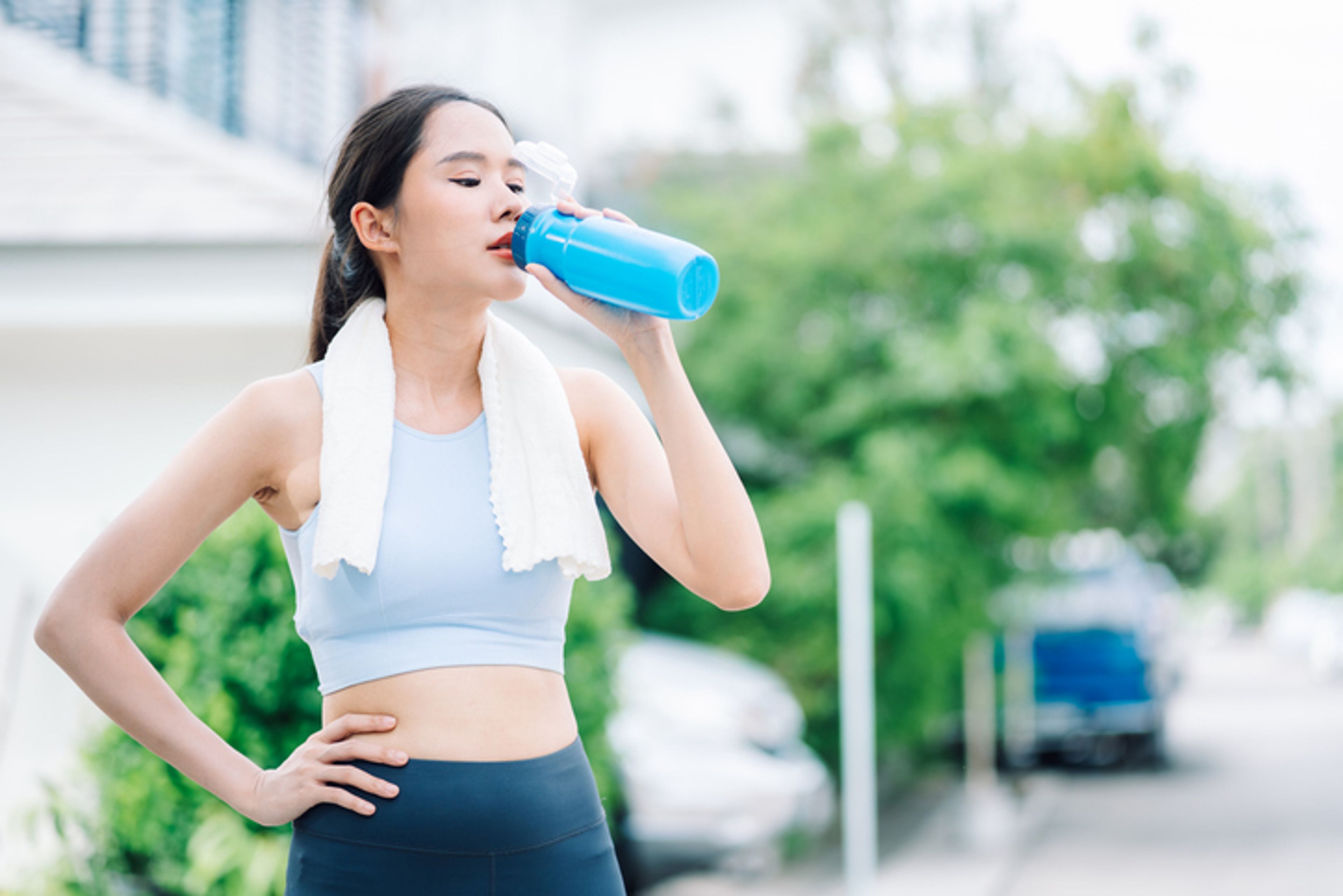 Young beautiful Asian woman in good health wearing a sports uniform is drinking water from a bottle after jogging from the park and running around the village.