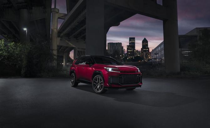 A red Toyota RAV4 parks under a bridge in an urban area with its headlights on