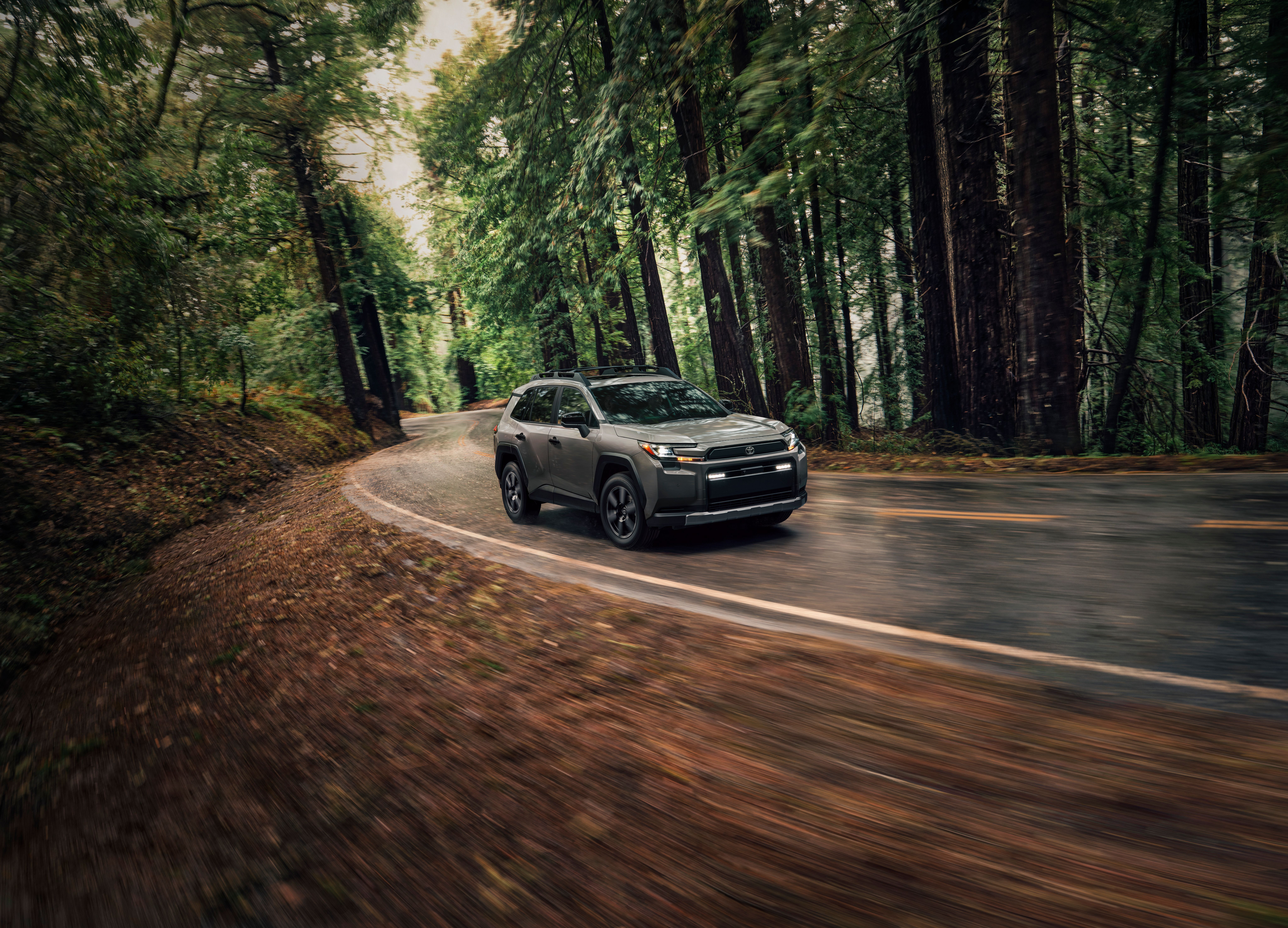 A 2026 Toyota RAV4 drives through a wooded area.