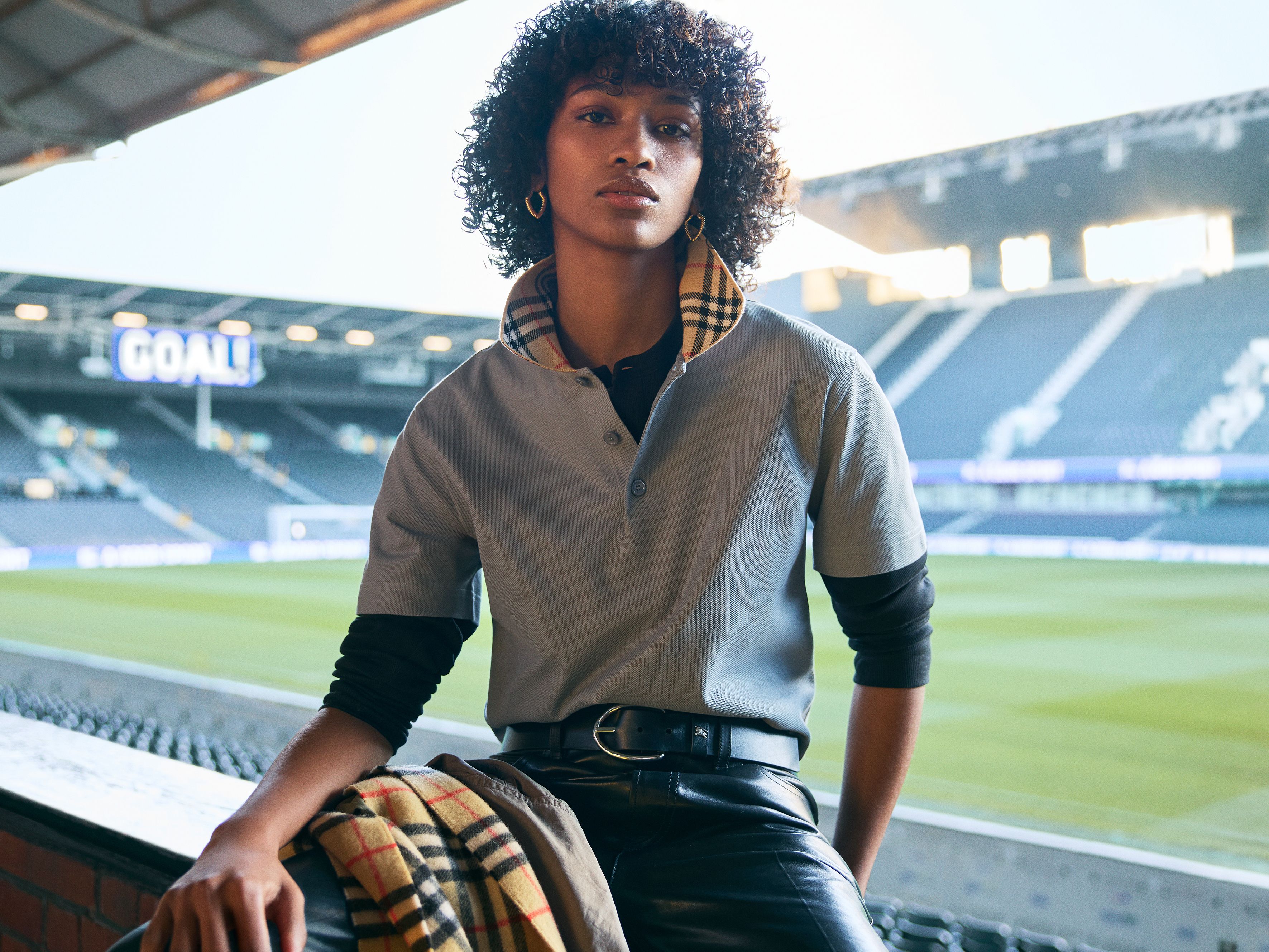 Model poses in front of a soccer pitch wearing a Burberry check top and scarf