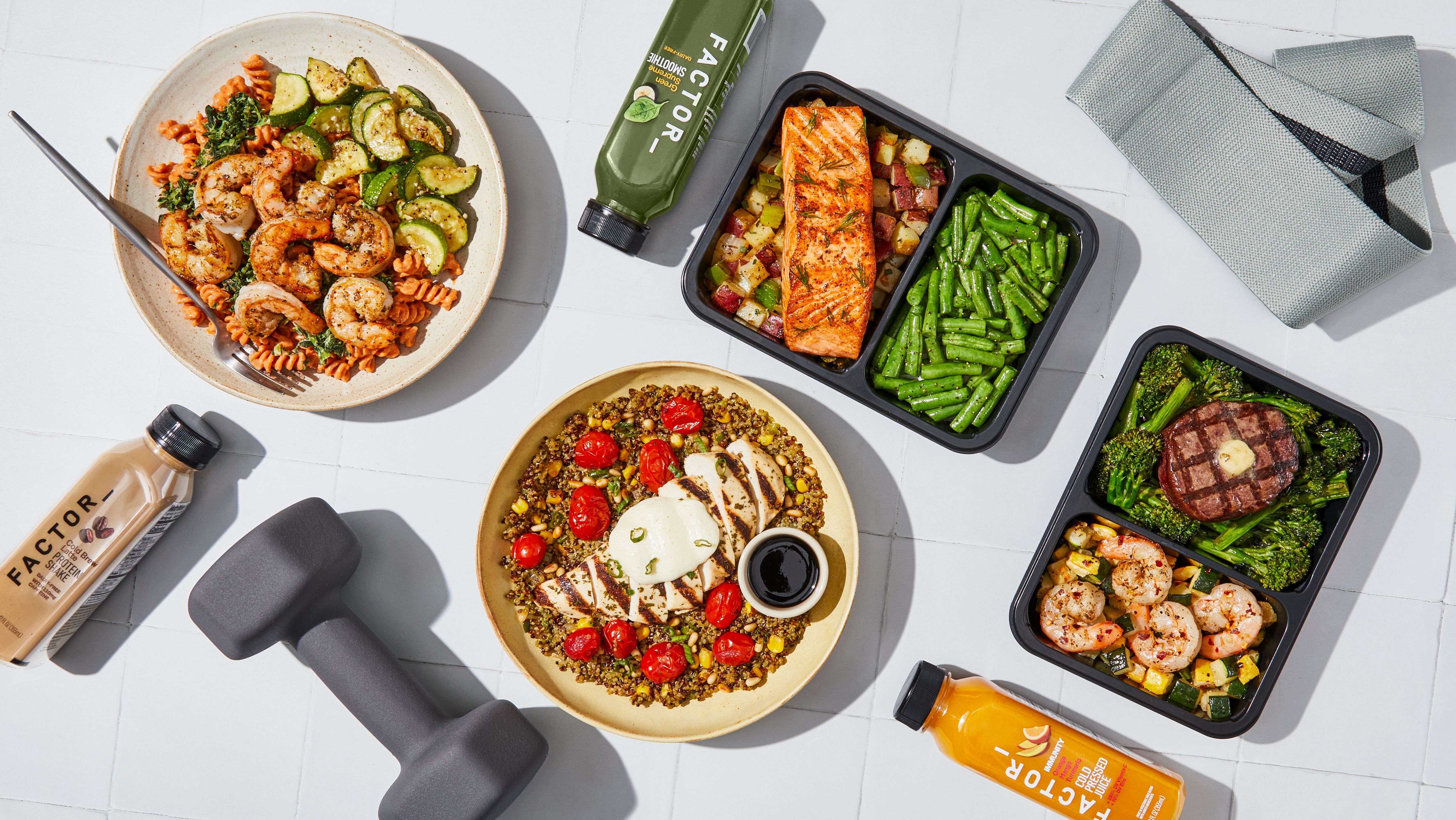 Factor meals are shown laid out on a table with workout and wellness equipment.