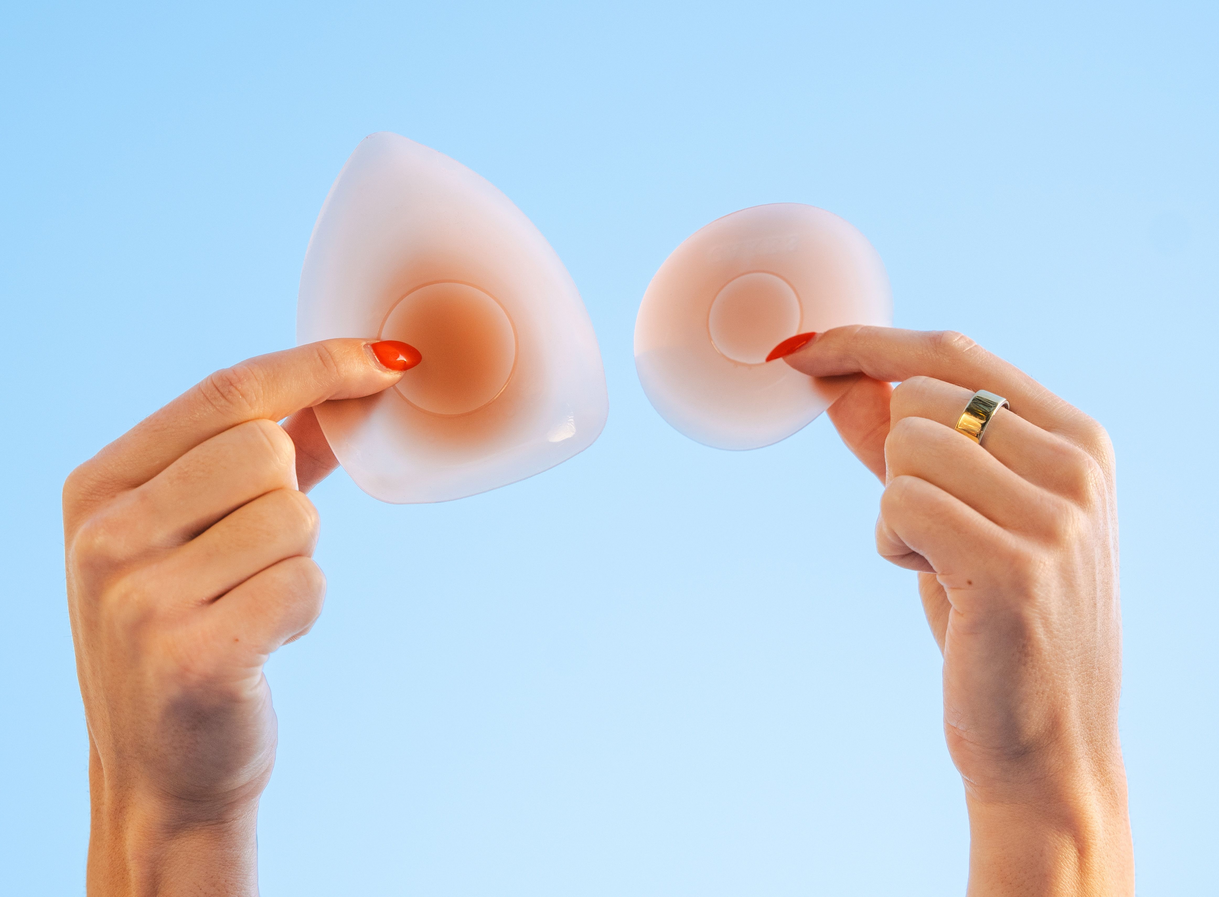 Two hands hold Cakes Body Sticky Cakes silicone covers against a light blue background, demonstrating their shape and flexibility.