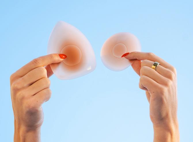 Two hands hold Cakes Body Sticky Cakes silicone covers against a light blue background, demonstrating their shape and flexibility.