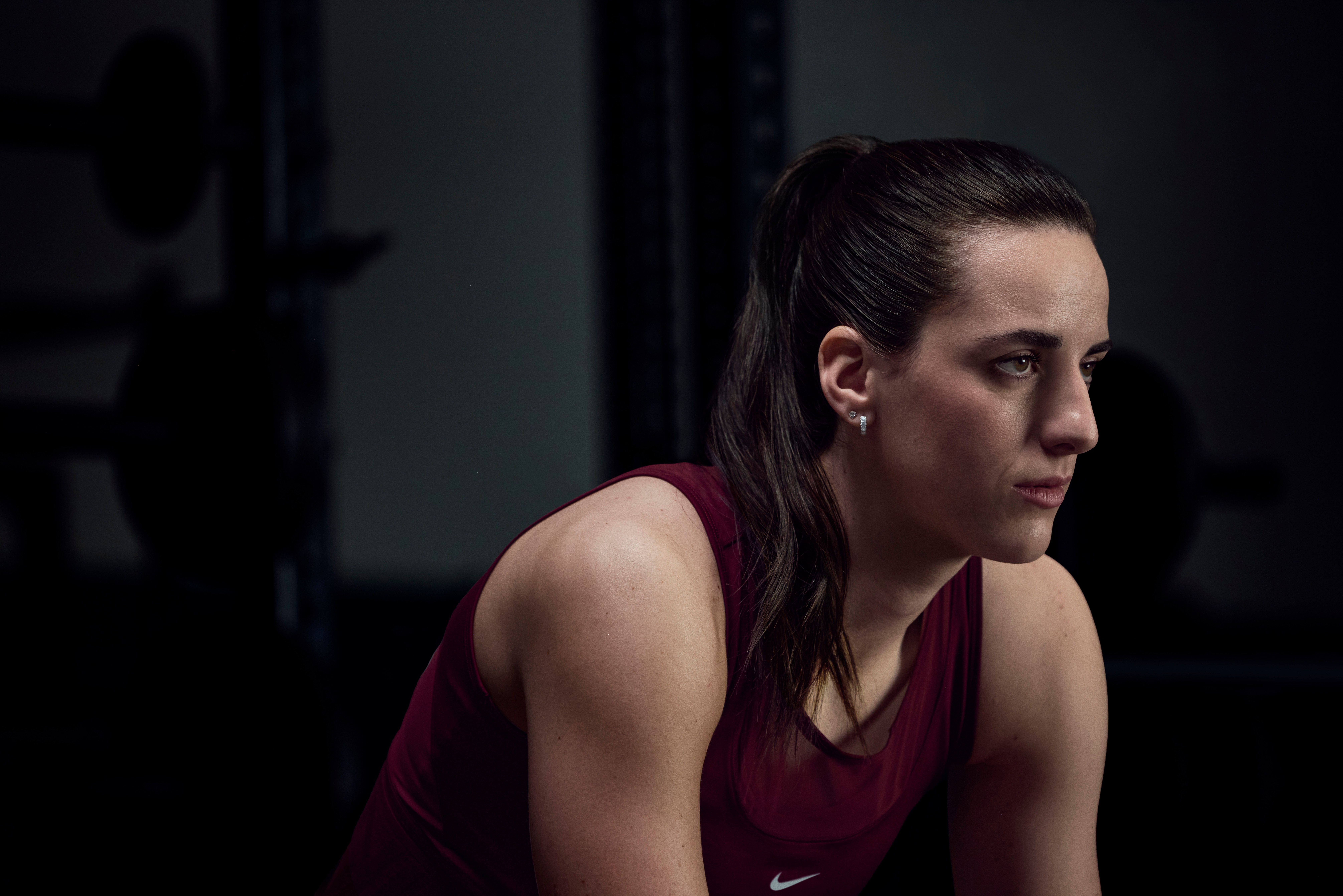 Caitlin Clark poses in a basketball gym in red athletic wear