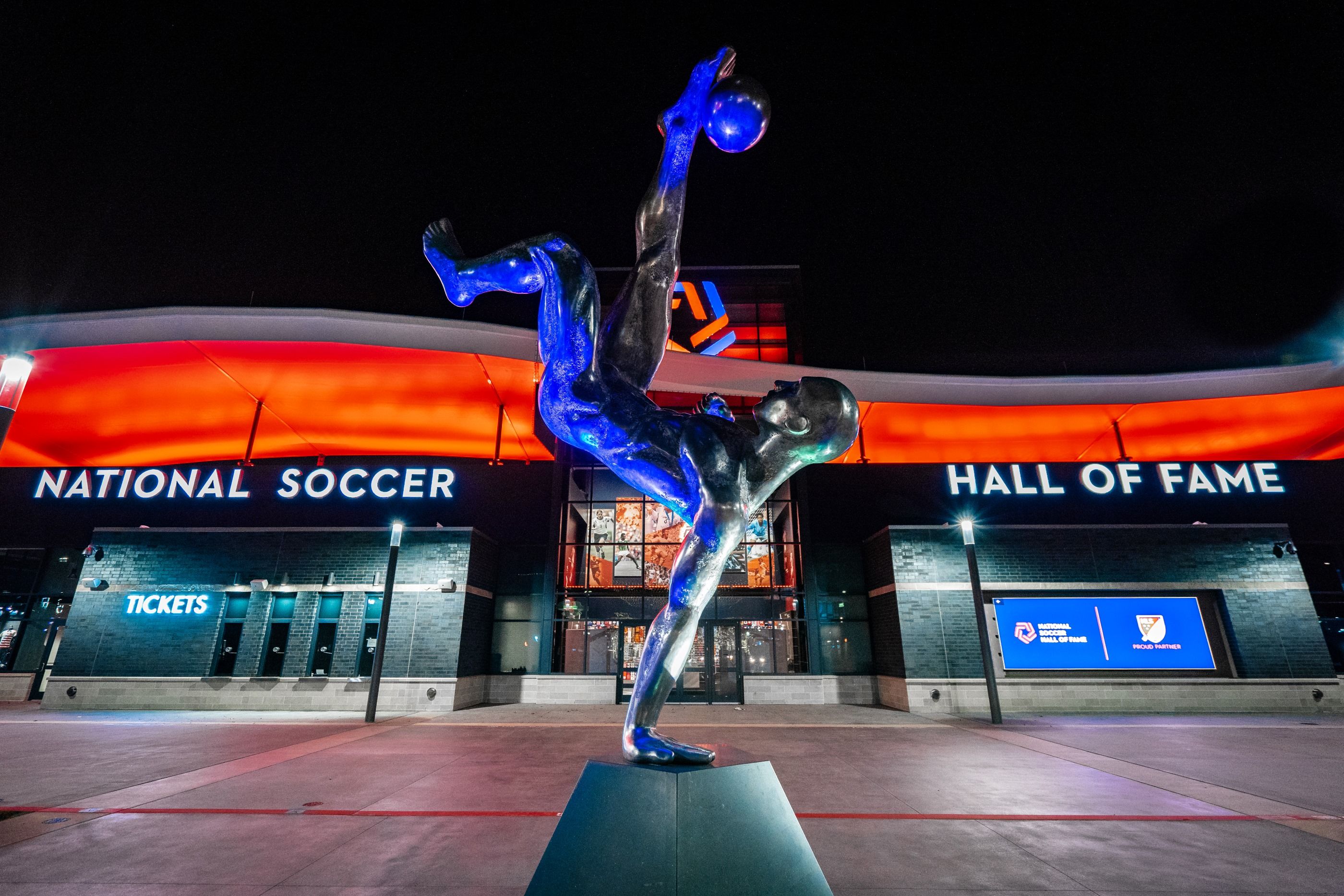 Statue of a soccer player performing a bicycle kick outside the National Soccer Hall of Fame at night.