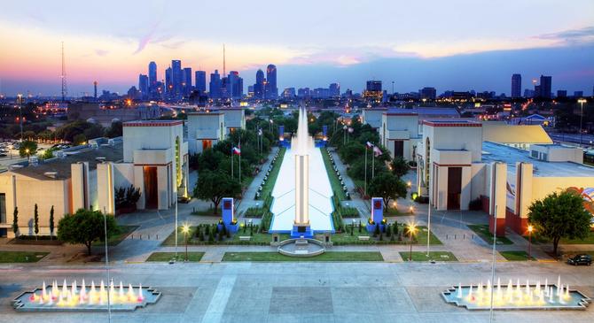 Aerial view of Fair Park in Dallas at dusk with the city skyline in the background.
