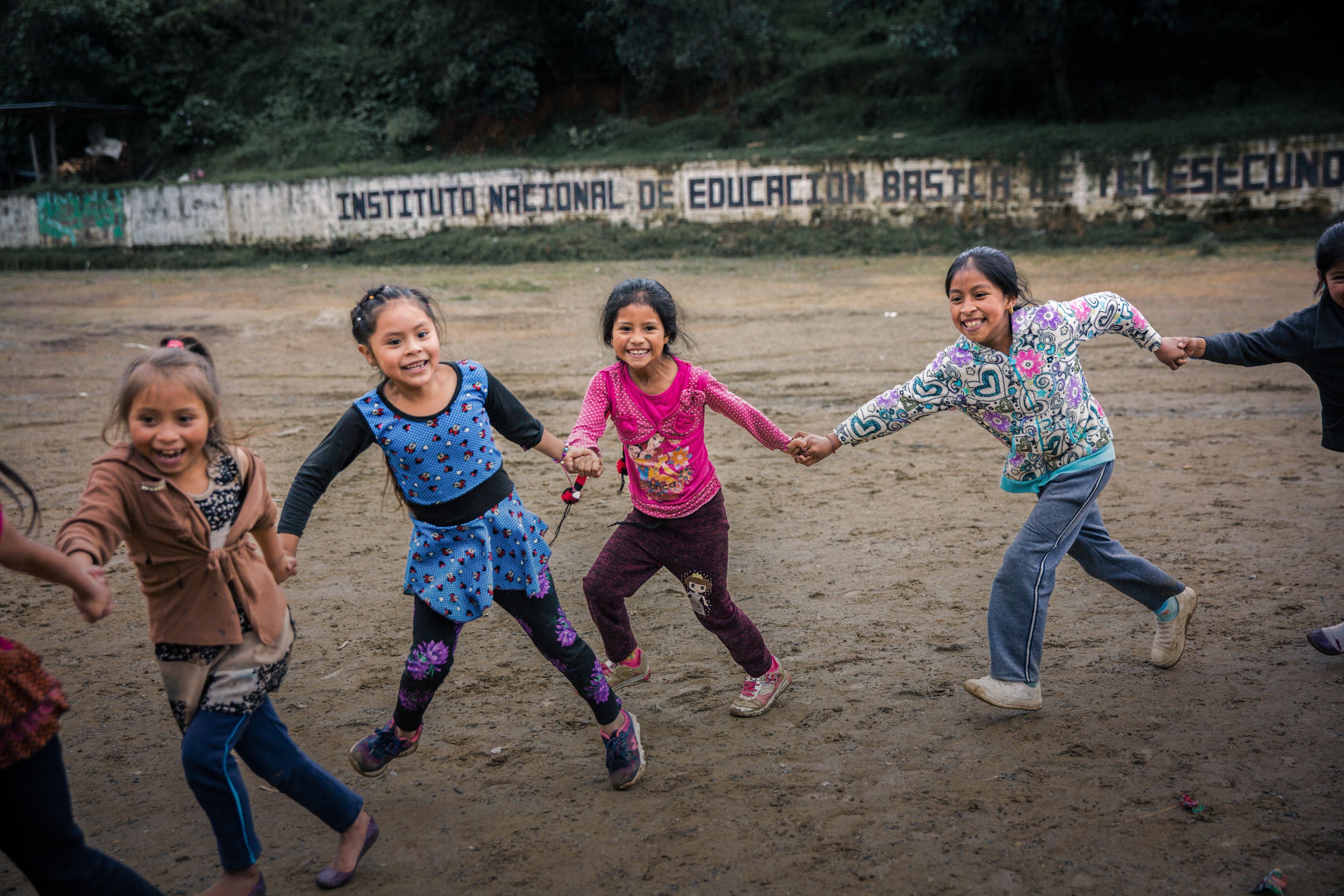 Children linking hands and playing in a sandy field