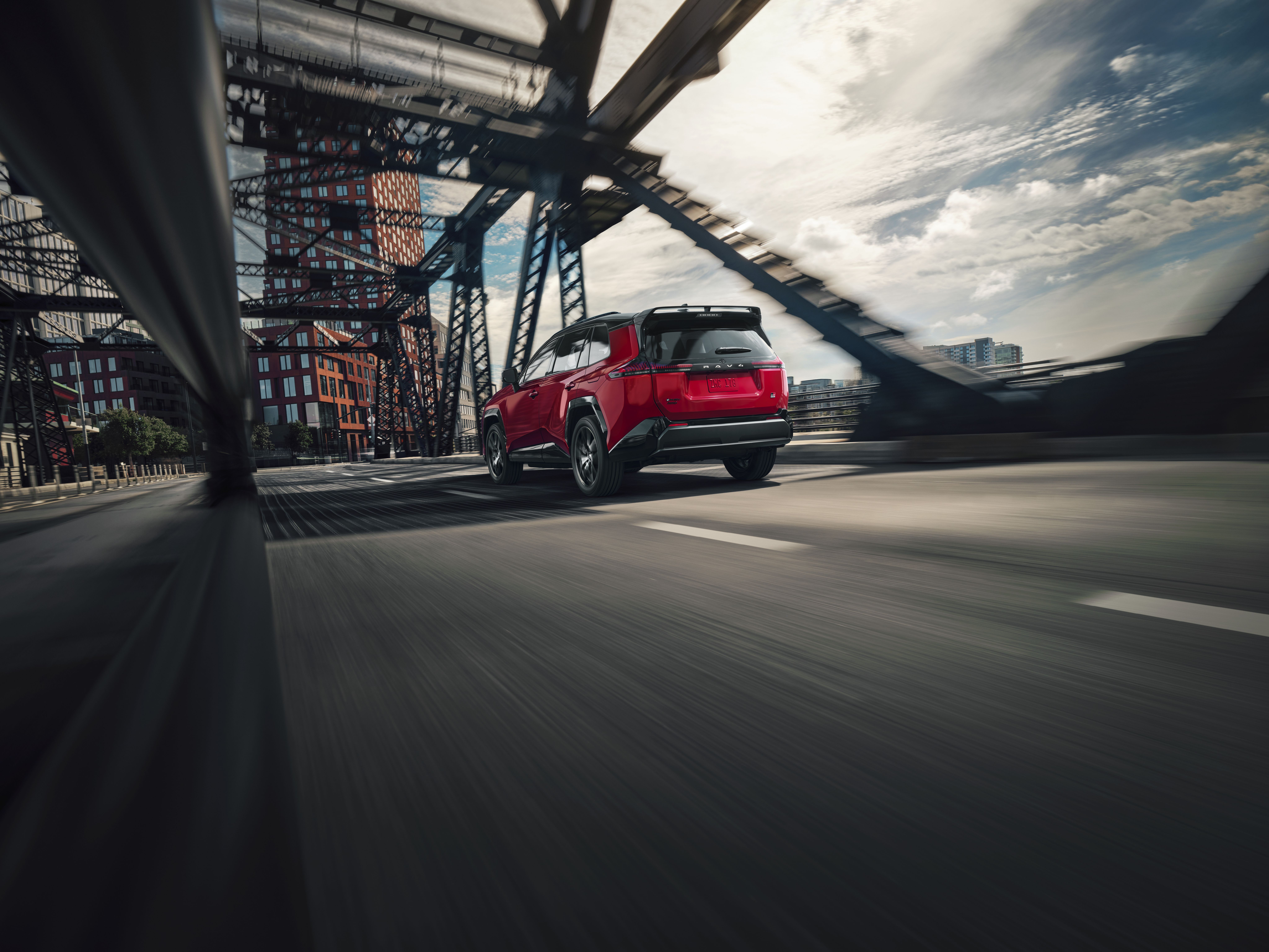 A red 2026 Toyota RAV4 drives on an urban bridge