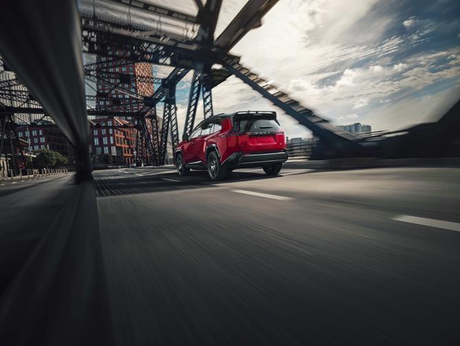 A red 2026 Toyota RAV4 drives on an urban bridge