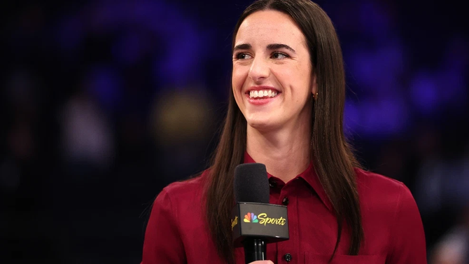 Caitlin Clark holds a microphone and smiles.