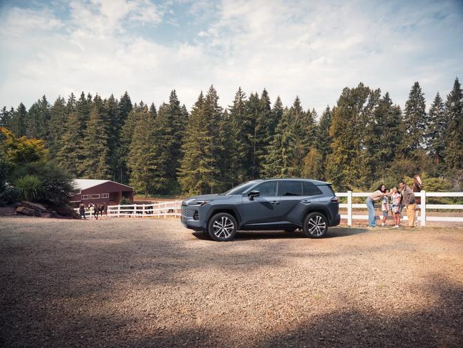 Toyota RAV4 parked on a gravel lot beside a horse farm, with a family gathered by a white fence and horses in the background.