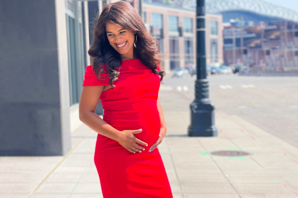 A pregnant woman wearing a red dress holds her belly.