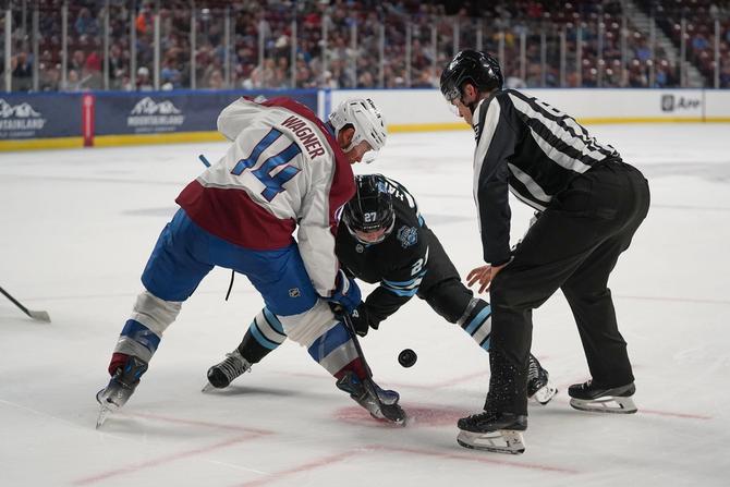 A linesman dropping the puck in front of two hockey players in a face off