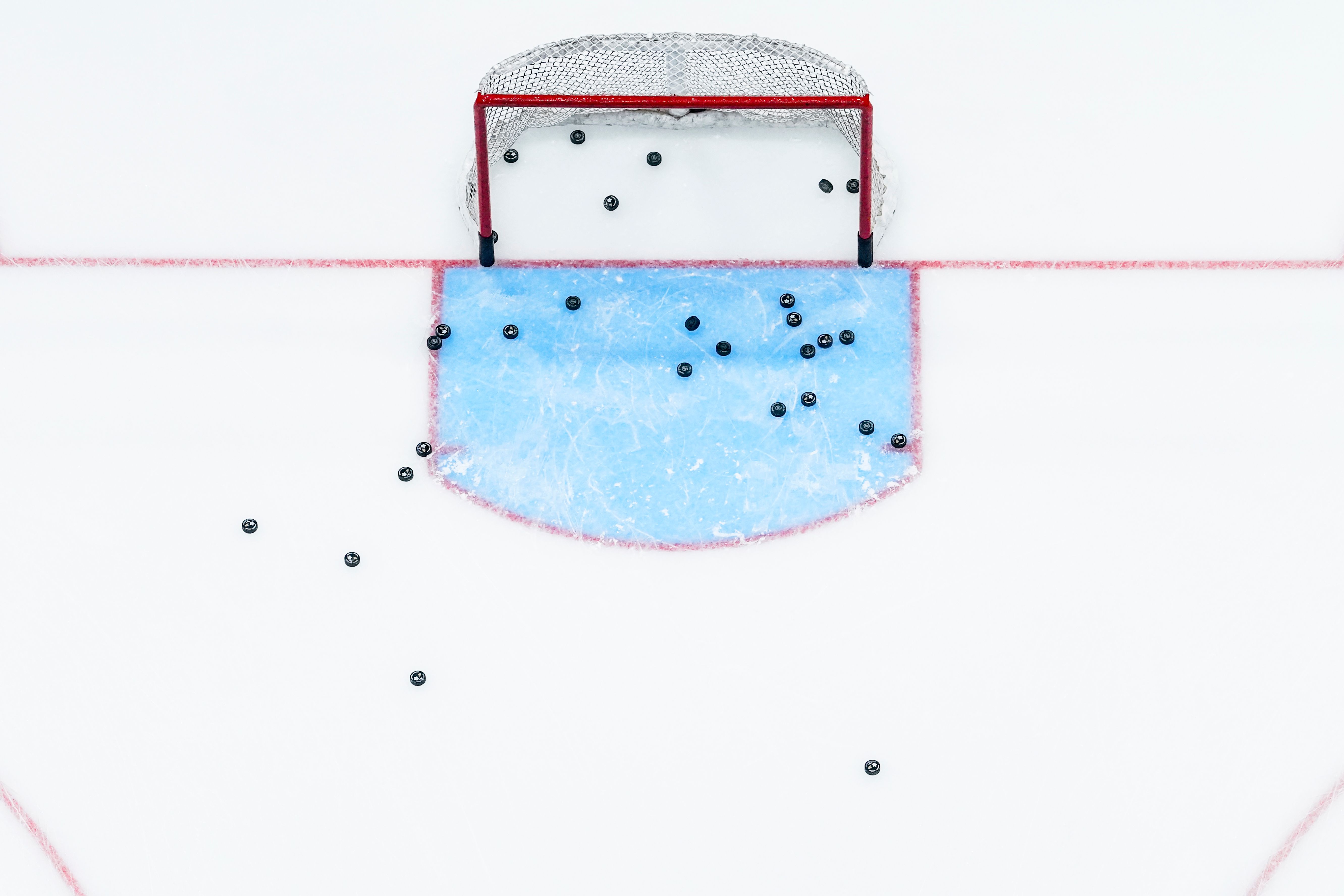 Bird's eye view of an ice hockey net with multiple pucks scattered.