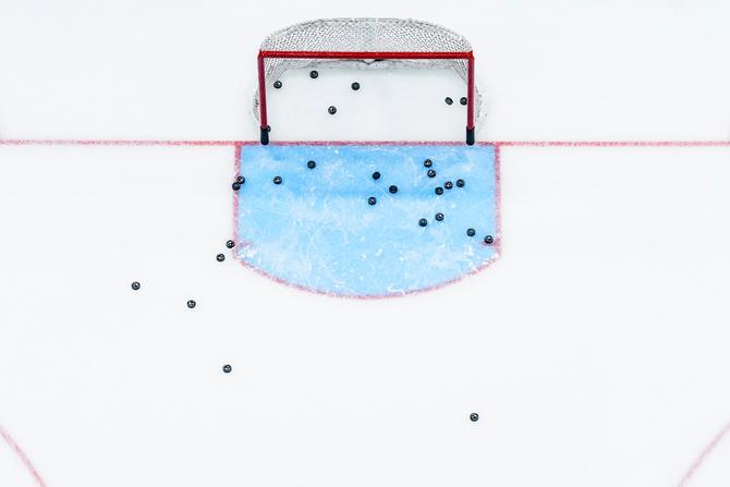 Bird's eye view of an ice hockey net with multiple pucks scattered.