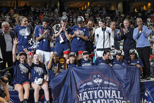 UConn players and coaches pose with the championship trophy and banner after defeating South Carolina in the national championship game.